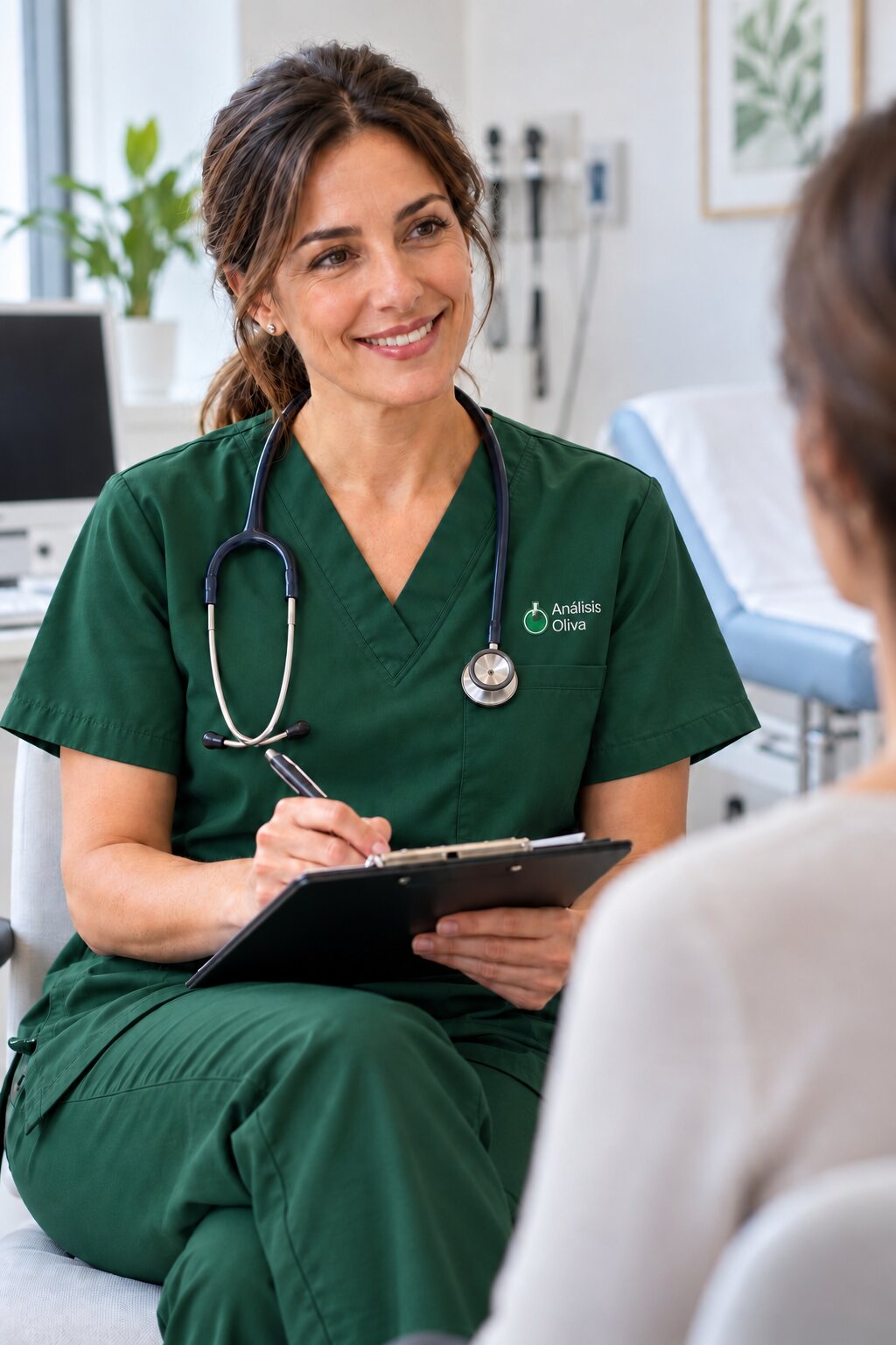 Médica con uniforme verde corporativo medio y un bordado discreto de Análisis Oliva tomando notas durante una consulta